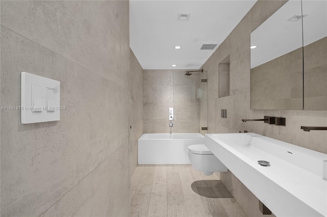 bathroom with toilet, tiled shower / bath, hardwood / wood-style flooring, and tile walls