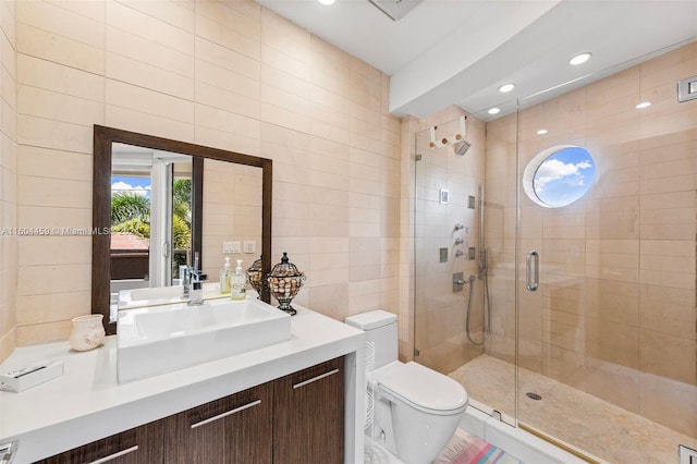 bathroom with tile walls, a shower with shower door, vanity, and toilet