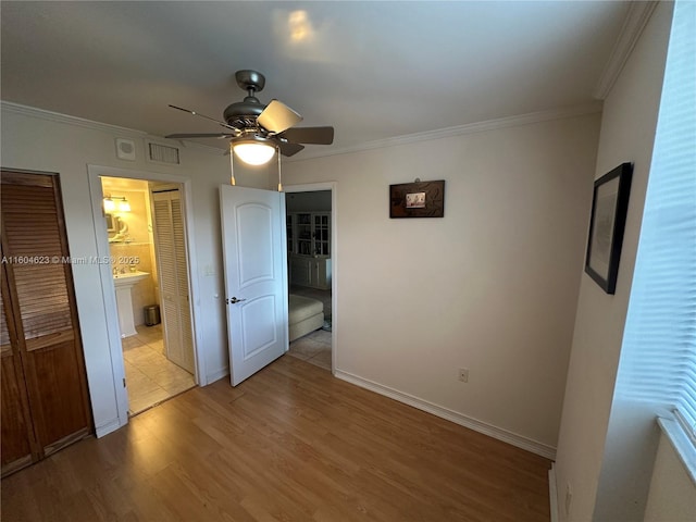 unfurnished bedroom with light wood-type flooring, ceiling fan, ornamental molding, and ensuite bath