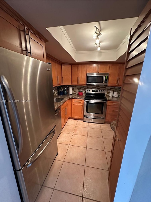 kitchen featuring dark stone countertops, light tile patterned flooring, a tray ceiling, stainless steel appliances, and ornamental molding