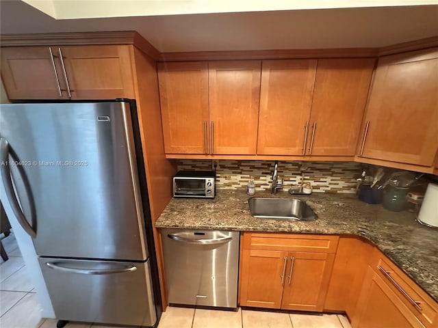 kitchen featuring decorative backsplash, sink, appliances with stainless steel finishes, light tile patterned floors, and dark stone counters