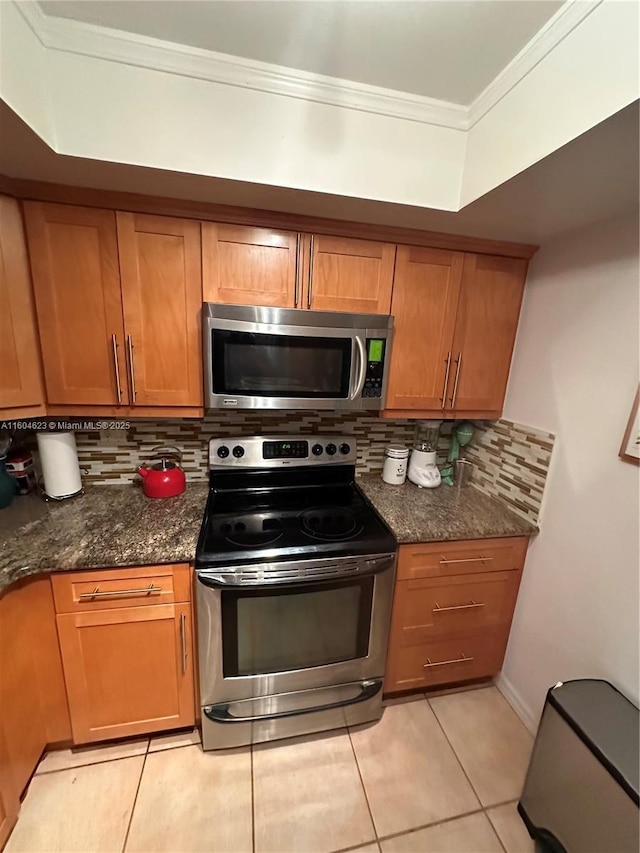 kitchen with light tile patterned floors, appliances with stainless steel finishes, dark stone countertops, and ornamental molding