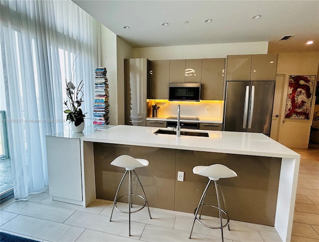 kitchen featuring a kitchen breakfast bar, stainless steel appliances, light tile floors, sink, and a kitchen island with sink