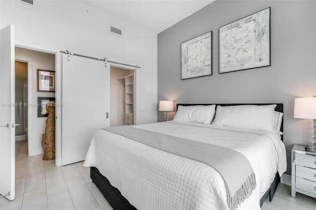 bedroom with a walk in closet, a barn door, light tile flooring, and a closet