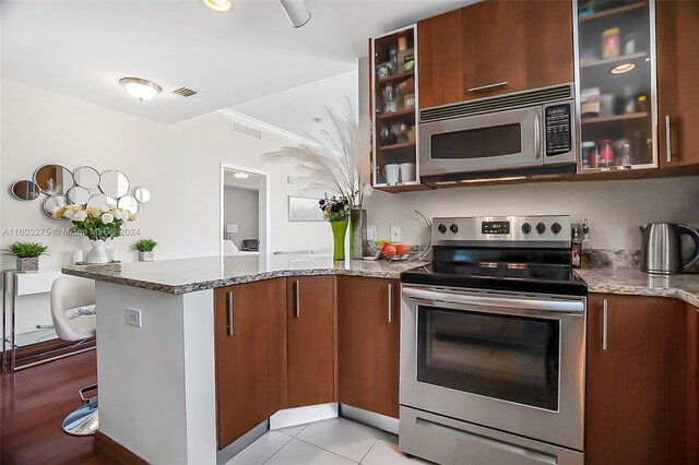 kitchen featuring kitchen peninsula, stainless steel appliances, crown molding, light stone countertops, and light tile floors