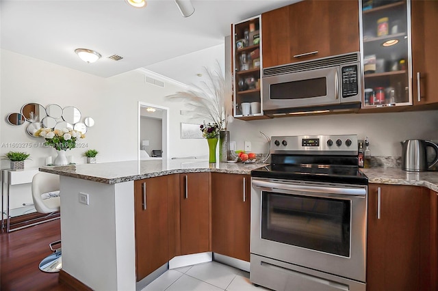 kitchen featuring light stone counters, a peninsula, visible vents, appliances with stainless steel finishes, and glass insert cabinets