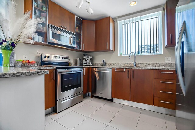 kitchen featuring stainless steel appliances, light stone counters, track lighting, light tile floors, and sink