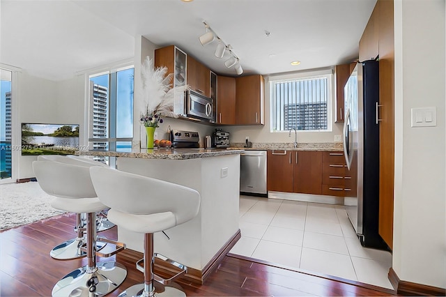 kitchen featuring a kitchen breakfast bar, stainless steel appliances, rail lighting, sink, and light tile floors