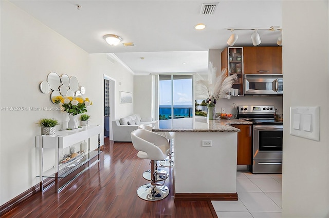 kitchen featuring stainless steel appliances, visible vents, brown cabinetry, glass insert cabinets, and a peninsula