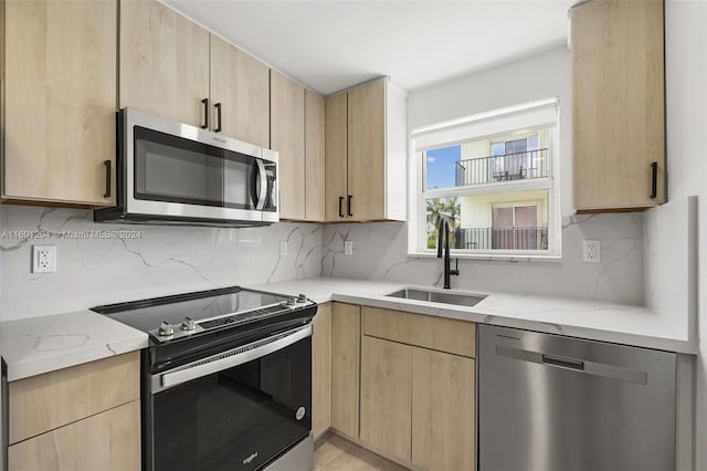 kitchen with backsplash, appliances with stainless steel finishes, sink, and light stone countertops