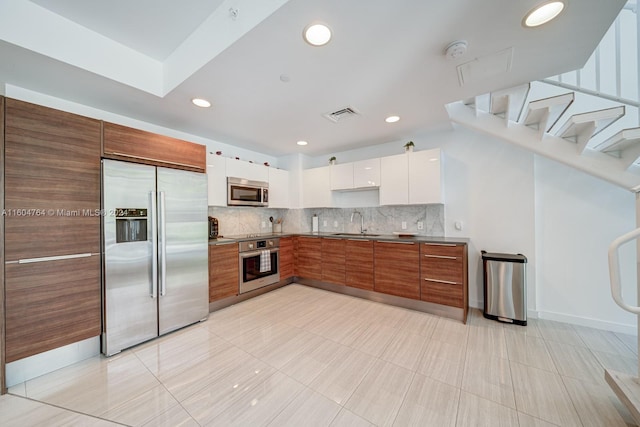 kitchen featuring appliances with stainless steel finishes, sink, light tile patterned floors, decorative backsplash, and white cabinetry