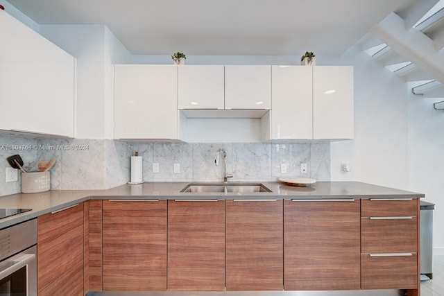 kitchen with white cabinetry, backsplash, stovetop, oven, and sink