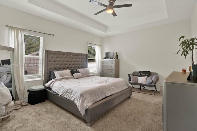 carpeted bedroom with ceiling fan and a tray ceiling