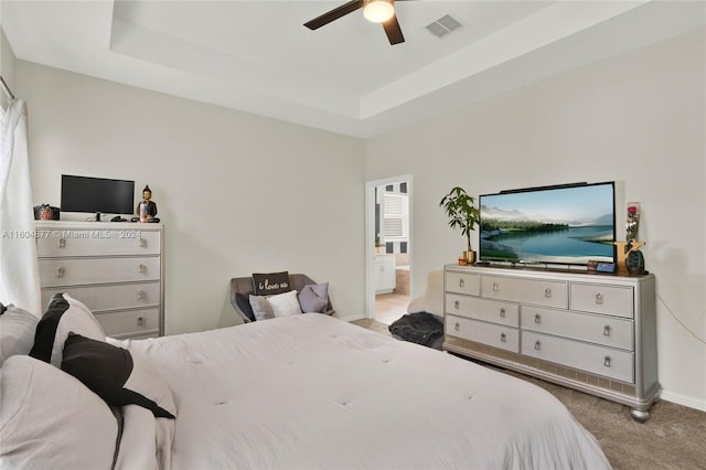 bedroom with a tray ceiling, carpet flooring, ceiling fan, and ensuite bath