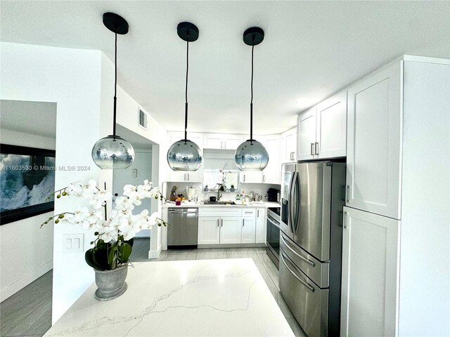 kitchen featuring hanging light fixtures, light stone countertops, white cabinetry, and appliances with stainless steel finishes