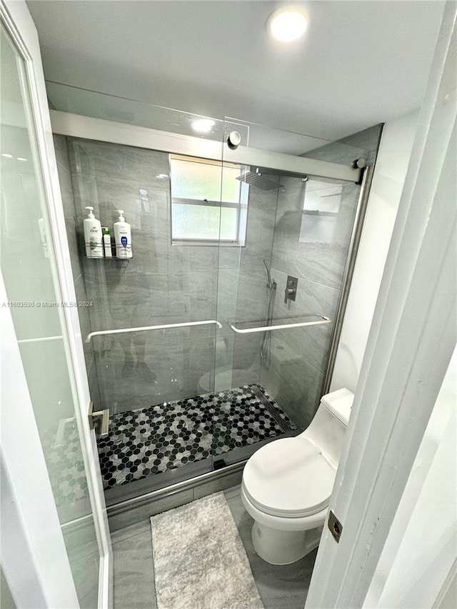 bathroom with tile flooring, toilet, and a shower with door