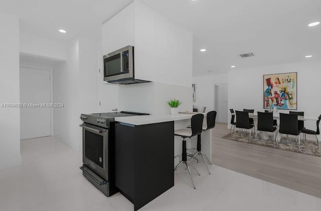 kitchen with light wood-type flooring, appliances with stainless steel finishes, and a kitchen breakfast bar