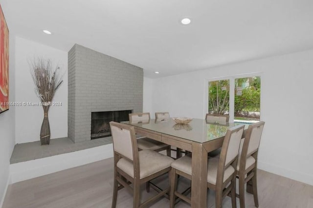 dining area with brick wall, light hardwood / wood-style flooring, and a fireplace