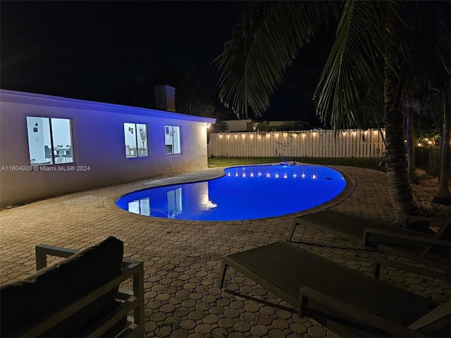 pool at night featuring a patio area