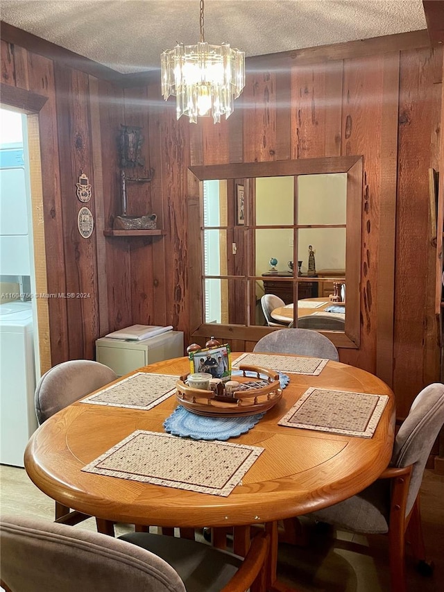 dining space with an inviting chandelier, stacked washer / dryer, a textured ceiling, and wood walls