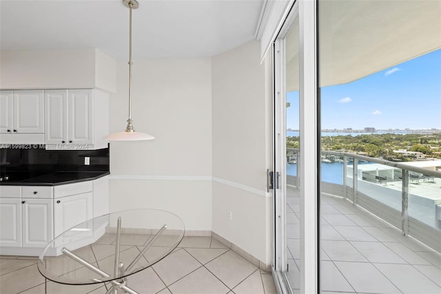 kitchen with pendant lighting, white cabinets, a water view, light tile patterned floors, and tasteful backsplash