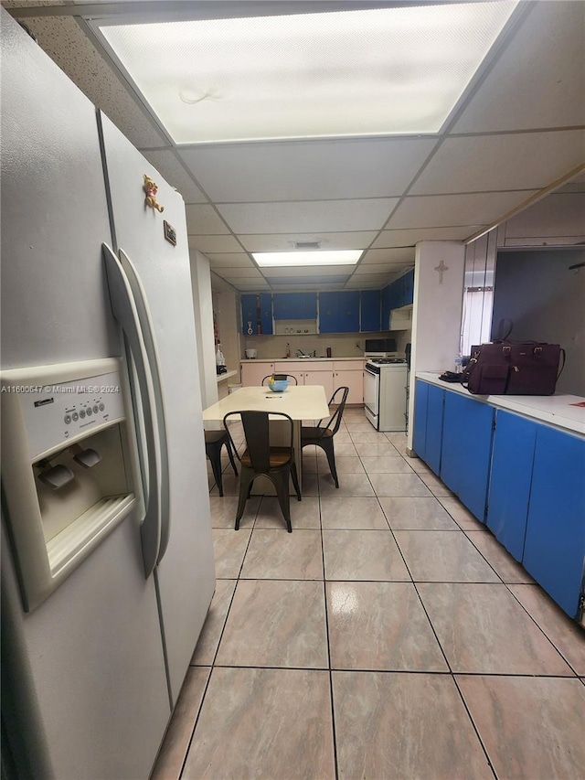 kitchen featuring blue cabinetry, white appliances, a paneled ceiling, and light tile patterned flooring