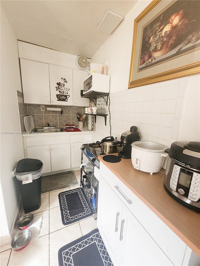 kitchen featuring stove, sink, decorative backsplash, light tile patterned floors, and white cabinetry