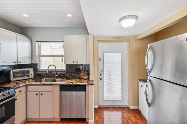 kitchen with light wood-type flooring, dark stone countertops, sink, white cabinetry, and appliances with stainless steel finishes