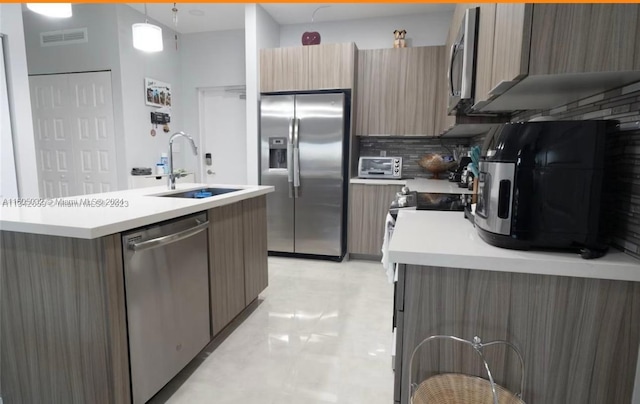 kitchen with an island with sink, sink, tasteful backsplash, and appliances with stainless steel finishes