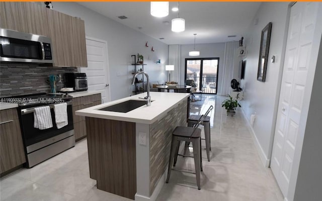 kitchen featuring a center island with sink, appliances with stainless steel finishes, backsplash, sink, and light tile floors