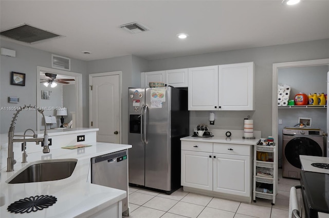 kitchen featuring washer / clothes dryer, stainless steel appliances, sink, light tile patterned floors, and white cabinetry