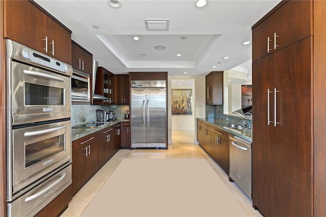 kitchen featuring backsplash, light tile floors, a raised ceiling, and built in appliances