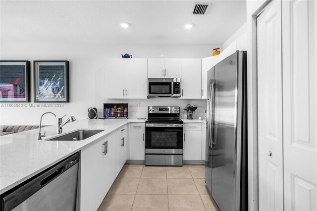 kitchen featuring white cabinets, stainless steel appliances, light stone countertops, sink, and light tile floors