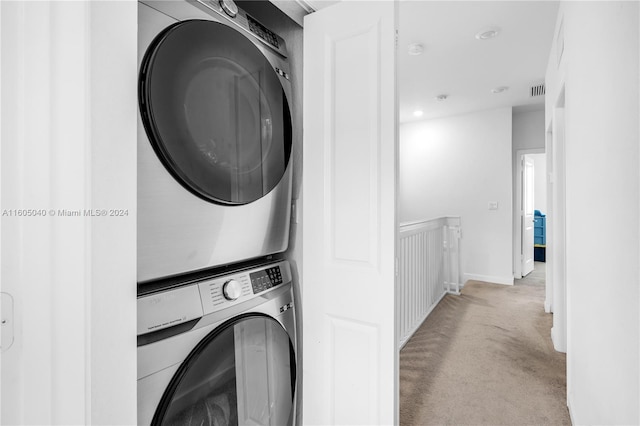 clothes washing area with laundry area, baseboards, stacked washer / dryer, and light colored carpet