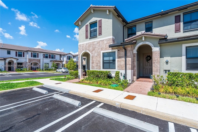 townhome / multi-family property with stone siding, a residential view, uncovered parking, and stucco siding