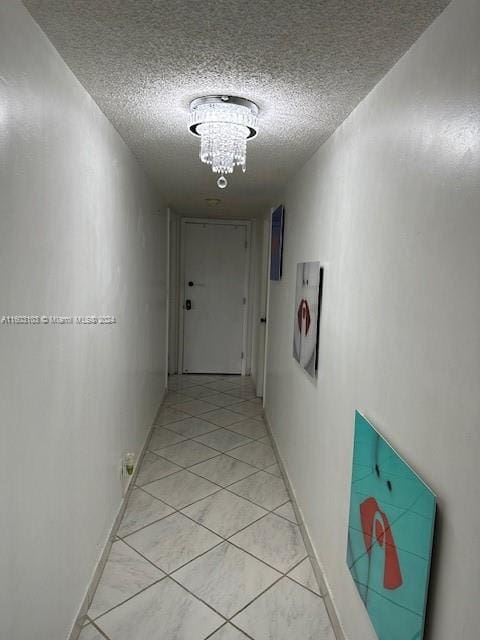 hallway with an inviting chandelier, a textured ceiling, and light tile patterned floors