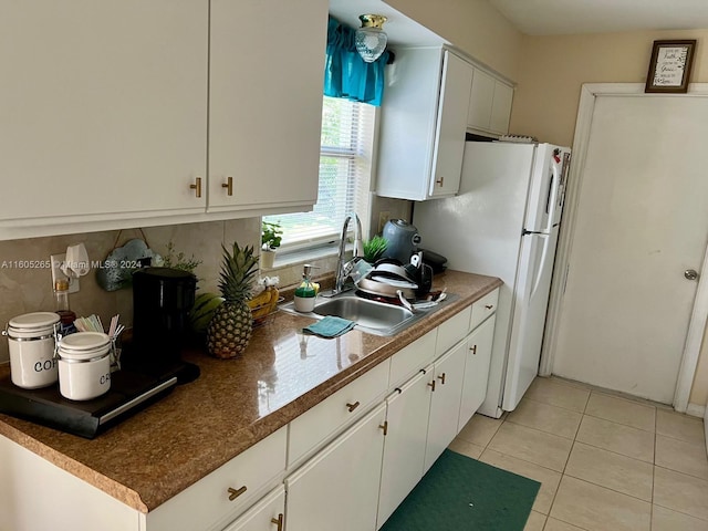 kitchen with white refrigerator, backsplash, light tile floors, sink, and white cabinets