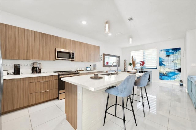 kitchen with a breakfast bar, a kitchen island with sink, stainless steel appliances, light tile patterned flooring, and decorative light fixtures