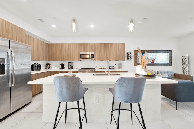 kitchen featuring stainless steel appliances, a center island with sink, a kitchen bar, and decorative light fixtures