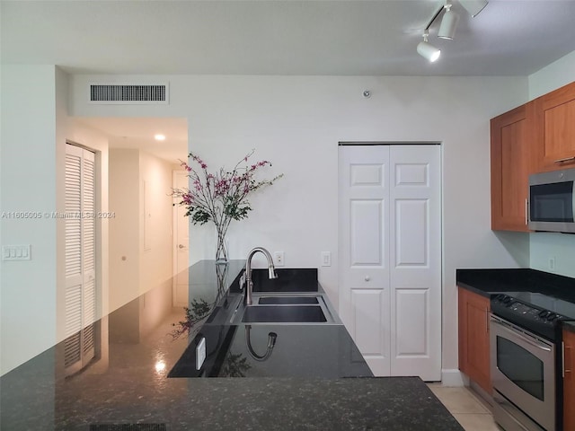 kitchen featuring rail lighting, dark stone counters, stainless steel appliances, sink, and light tile patterned floors