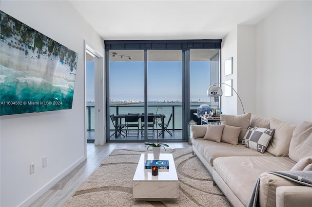 living room with floor to ceiling windows, a water view, and light hardwood / wood-style floors