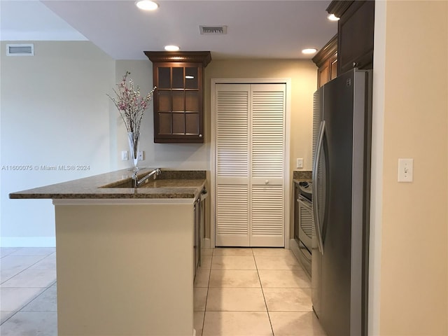 kitchen with dark brown cabinetry, kitchen peninsula, stainless steel fridge, and light tile flooring