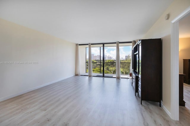 empty room with floor to ceiling windows, light wood-style flooring, and baseboards