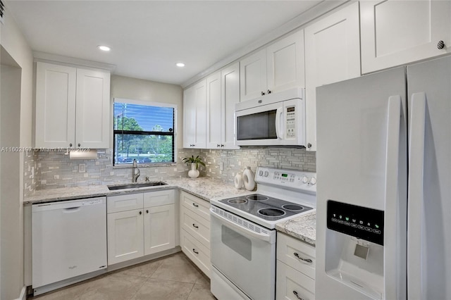 kitchen featuring white appliances, sink, light tile patterned floors, light stone counters, and white cabinetry