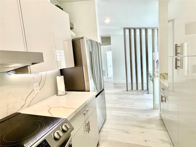 kitchen with white cabinets, ventilation hood, light stone countertops, light wood-type flooring, and appliances with stainless steel finishes