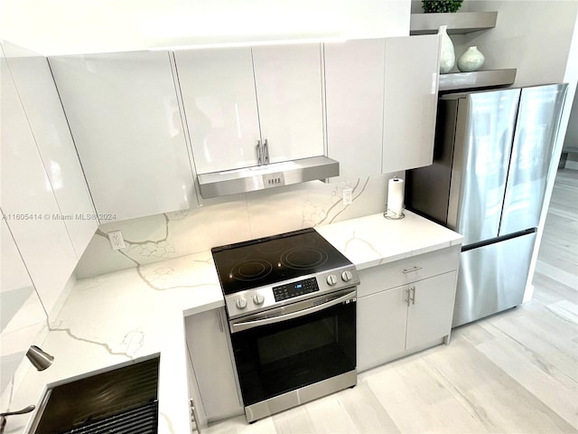 kitchen featuring backsplash, white cabinets, light hardwood / wood-style floors, light stone counters, and stainless steel appliances