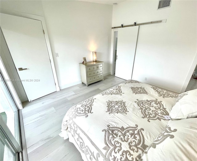 bedroom featuring a barn door, light wood-type flooring, and a closet