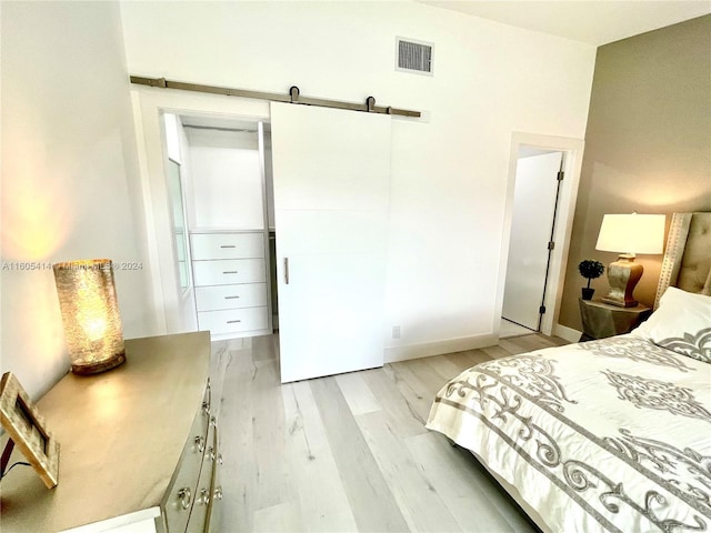 bedroom with a barn door, light wood-type flooring, and a closet