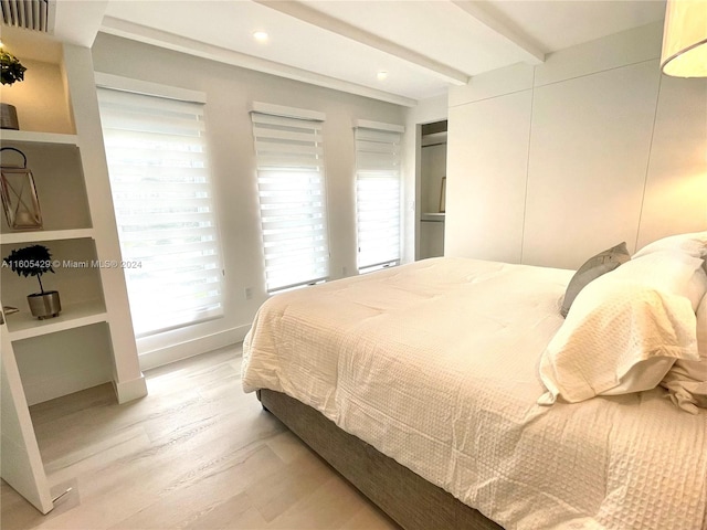 bedroom featuring beam ceiling, light hardwood / wood-style floors, and multiple windows