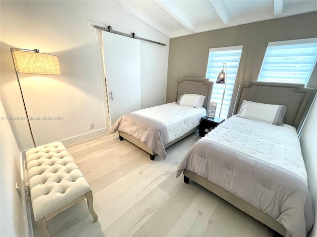 bedroom with a barn door, light hardwood / wood-style flooring, and vaulted ceiling with beams